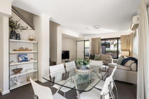 Una sala de estar con una mesa de cristal y sillas blancas. en Apartment 46, en Margaret River Town