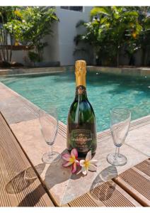 a bottle of wine and two glasses next to a swimming pool at Villa Emeraude in Saint-Louis
