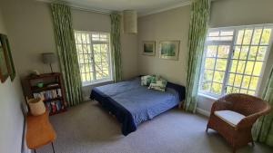 a bedroom with a bed and a chair and windows at Tranquil Stylish Home with Nature Pool near Reserve in Somerset West