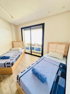 two beds in a room with a large window at Mehdia's Paradise in Kenitra