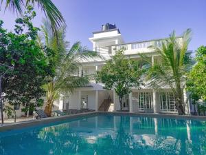 a swimming pool in front of a house with palm trees at Escape Hole in Diani Beach