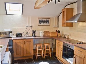 Una cocina con gabinetes de madera y un mostrador con taburetes. en The Old Stable, en Holywell Bay