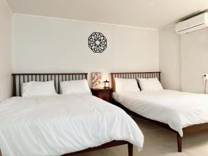 Dos camas en un dormitorio con sábanas blancas y un reloj. en Arang Stay Seoul 동대문, en Seúl