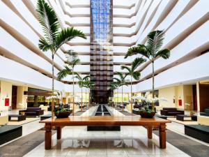 a large lobby with a table and palm trees at Apartamento Suites Le Jardin Caldas Novas Goiás in Caldas Novas