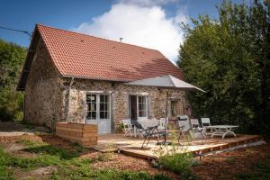 a stone house with a deck with chairs and an umbrella at L'arbres aux minutes in Saint-Martin-Sepert