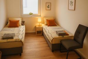 two beds in a room with a chair and a window at Wohnen am See in Zernsdorf