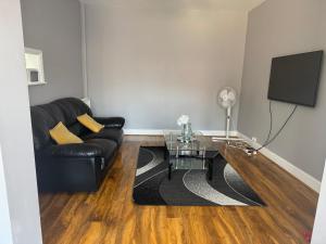 un soggiorno con divano in pelle nera e TV di Westwick Gardens Retreat - 4 Bedroom House a Hounslow