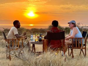three people sitting at a table watching the sunset at Furaha Luxury Lodge in Mto wa Mbu