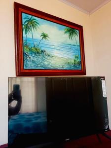 a painting of a beach with palm trees behind a computer monitor at inya lodge in Ciudad Cortés