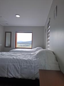 a bedroom with a white bed and a window at Cabañas Horizonte Sur in Coihaique +1 photo