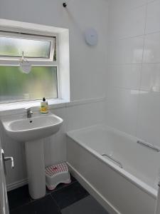 a white bathroom with a sink and a bath tub at 3-bedroom home with large garden and free parking in Loughton