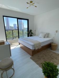 a white bedroom with a bed and a large window at Ap na Brava in Itajaí