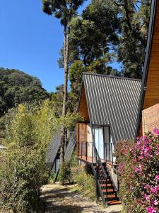 ein Haus mit Metalldach und Treppen neben Blumen in der Unterkunft Chalé Mon Amour 2, onde o amor se encontra, 2 min do Capivari in Campos do Jordão