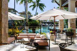 an outdoor patio with tables and umbrellas and a pool at Tranquil Waters 2 Bedroom Apartment in Port Douglas