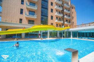a man in a swimming pool with a slide in a building at Britannia Resort & SPA in Vlorë
