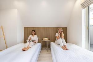 Zwei Frauen sitzen auf Betten und telefonieren mit ihren Handys. in der Unterkunft STAY ARI Higashishinjuku in Tokio