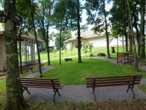 two benches in a park with trees and a building at Quiosque Golf Santa Cruz do Sul in Santa Cruz do Sul