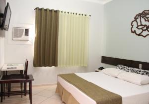 a bedroom with a bed and a table and a window at Novo Hotel Herta in Guaíra