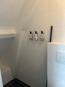 a white tiled bathroom with three bottles on a shelf at Cozy apartment in Enschede