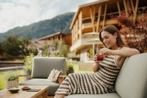 a woman sitting on a chair holding a drink at Taubers Bio Vitalhotel in Chienes