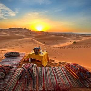 a table in the desert with the sunset in the background at Eternal Luxury Camp in Merzouga