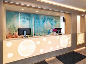 a hotel lobby with a reception counter with two monitors at B&B Hotel Wolfsburg-Weyhausen in Wolfsburg