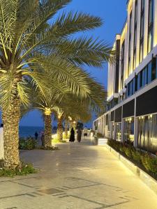 a row of palm trees on a sidewalk next to a building at By The Beach - Prime location in Sarūq