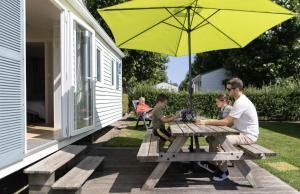 a man and two children sitting at a picnic table with an umbrella at Vakantiepark Klein Strand - Comfort Chalet 6p in Jabbeke