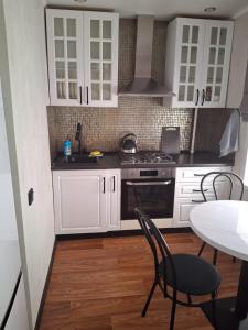 a kitchen with white cabinets and a stove and a table at Уютная 2-х комнатная квартира in Rudny