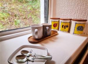 Un mostrador con dos tazas y cucharas al lado de un fregadero. en Rock Cottage, en Isle of Arran