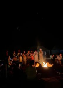 a group of people standing around a fire in the dark at Aka luxury camp in Merzouga