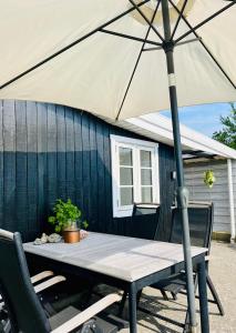 a picnic table with an umbrella in front of a house at Summer Cottage Idyll In Charming Karrebæksminde! in Karrebæksminde