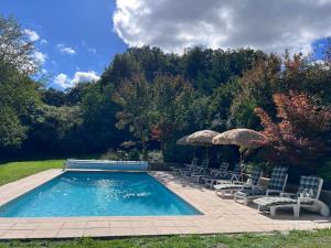 a swimming pool with chairs and umbrellas at Wisteria cottage in Bersac-sur-Rivalier