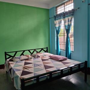 a bed in a room with a green wall and a window at Atithi Homestay in Sivasagar