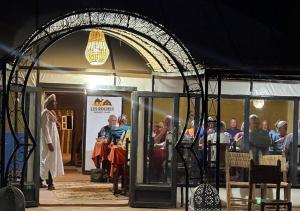 a group of people sitting at tables under an archway at Les Roches Desert Camp in Merzouga
