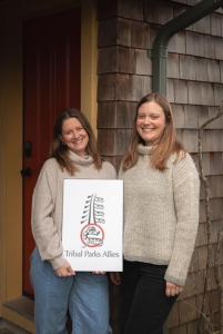 due donne in piedi l'una accanto all'altra con un cartello di South Swell Tofino (formerly Blue Heron Waterfront Home amid Old Growth Cedars) a Tofino