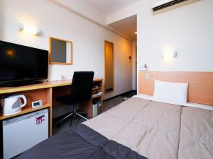 a bedroom with a bed and a desk with a television at Super Hotel Minamata in Minamata