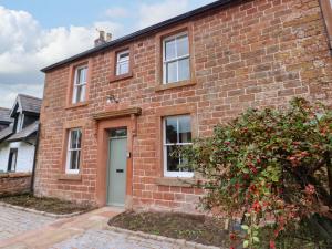 a brick house with a white door and a bush at Milford in Great Corby