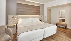 a bedroom with a large white bed and a chair at NH Córdoba Califa in Córdoba