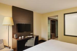 a hotel room with a bed and a desk and a tv at NH Stuttgart Airport in Filderstadt