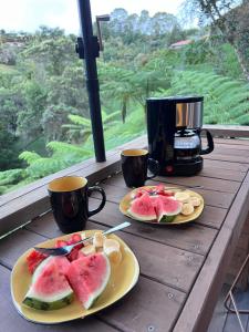 Dos platos de fruta en una mesa de madera con dos tazas. en Chalet Boutique a 7 Min del Aeropuerto JMC, en Guarne