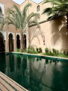 a swimming pool in front of a building with palm trees at Riad 29 Mouassine in Marrakech