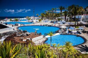 Una piscina en un resort con palmeras y el océano. en Lindo estudio en Martiánez, en Puerto de la Cruz