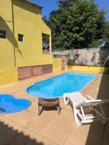 a swimming pool with a chaise lounge and a yellow building at Sítio vida boa - Jambreiro in Itabira
