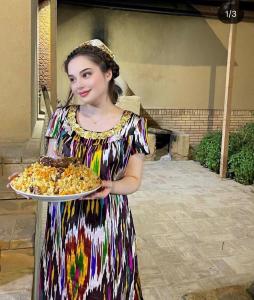 una donna in abito che tiene in mano un piatto di cibo di Hotel CHORMINOR 95 m to Bukhara Old Town Unesco Heritage List est-since 1697 a Bukhara