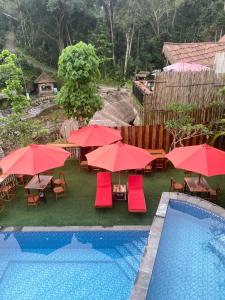 una piscina con sombrillas rojas, mesas y sillas en Infinity Villa and Resto, en Tembuku 7 fotos más