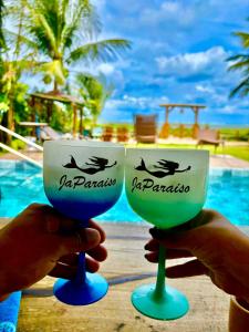 a person holding up two wine glasses in front of a pool at Ateliê JaParaíso in Japaratinga