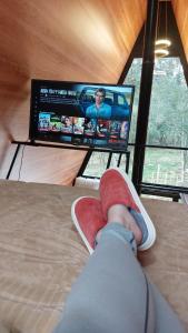 una persona acostada en una cama frente a una TV en Chalé Araucárias Cambará do Sul, en Cambará