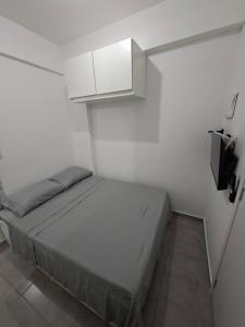a small white room with a bed and a cabinet at Studio Teresa - 200m UFSJ e Igreja São Francisco in São João del Rei