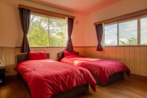 a bedroom with two red beds and a window at 軽井沢 デッキからの眺望 BBq カラオケ IC下車5分 in Karuizawa